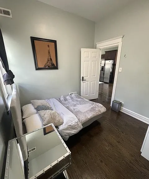 Furnished bedroom with a full-size bed, hardwood floors, and nearby access to the kitchen for added convenience.