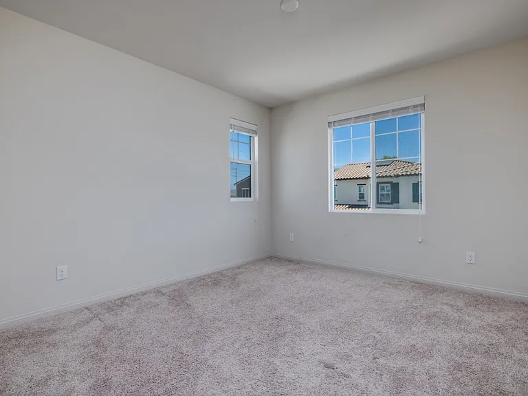 Second upstairs bedroom featuring soft carpet flooring and large east-facing windows that welcome plenty of natural morning light. A bright, peaceful space ideal for a guest room, office, or cozy retreat in this modern Menifee home.