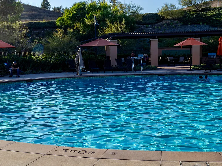Community Pool: View of the sparkling circular pool, part of an amenity package that includes an adjacent spa, outdoor shower, lounge umbrellas, and a premium BBQ setup.
