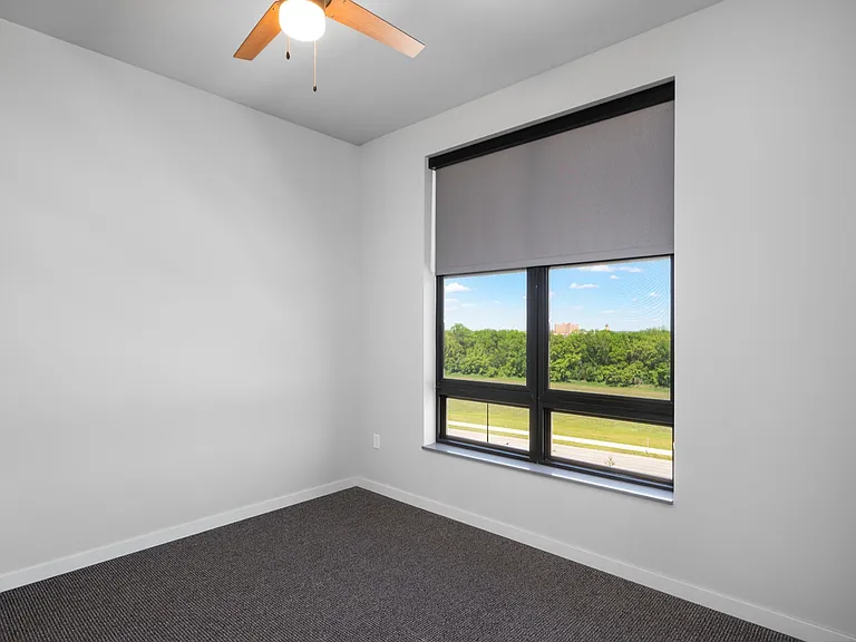 Bright, modern bedroom with a large window offering serene green views, complete with a stylish ceiling fan. Bright, modern bedroom with a large window offering serene green views, complete with a stylish ceiling fan.