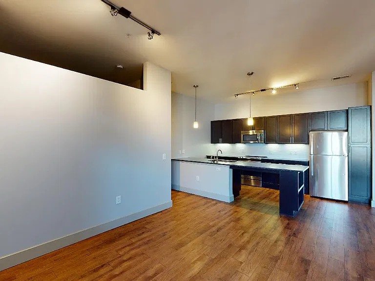 Apartment kitchen with stainless steel appliances, dining and living room with wood-style flooring.