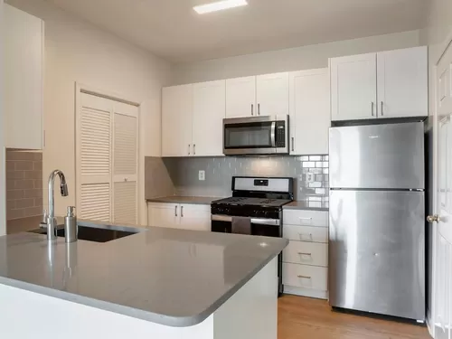 Renovated Package II kitchen with white cabinetry, grey quartz countertops, tile backsplash, stainless steel appliances, and hard surface flooring - Avalon Reston Landing