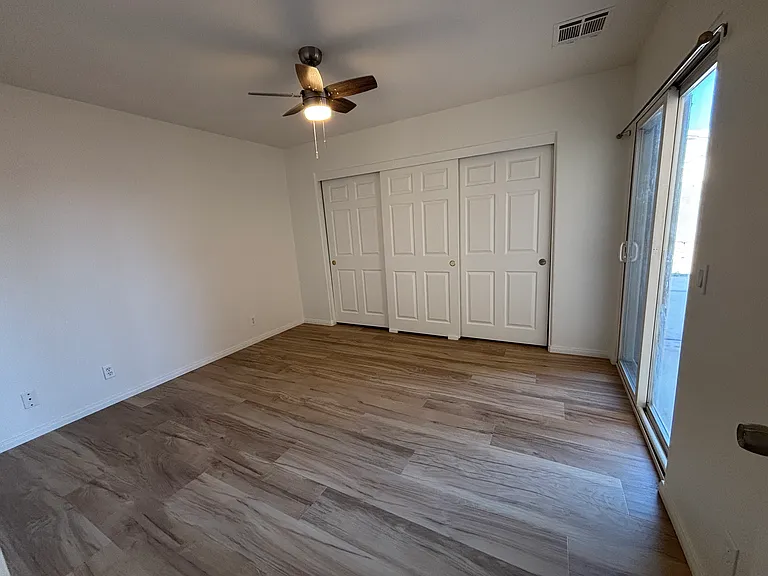 Bright bedroom with ceiling fan, double closet, durable flooring, and direct access to the backyard.