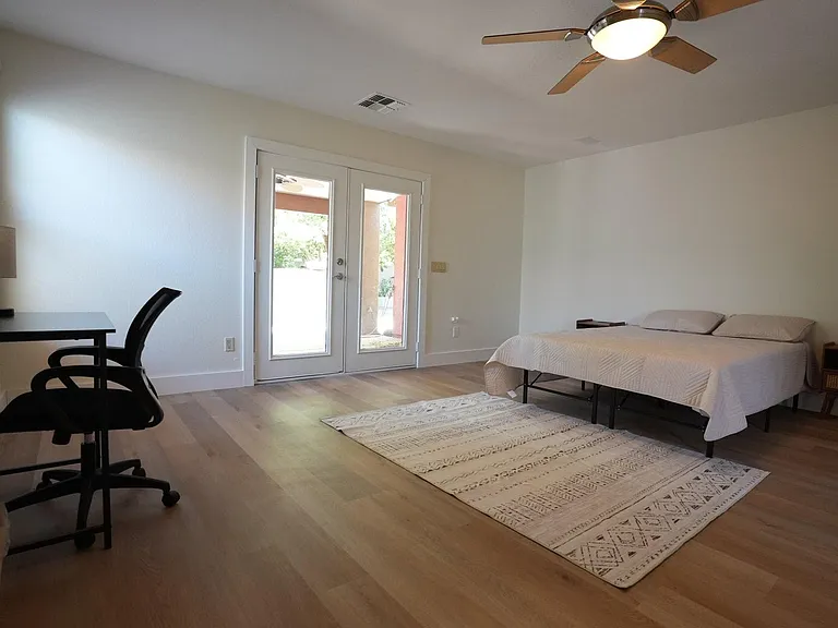 Spacious bedroom with wood-style flooring, ceiling fan, desk area, and French doors opening to an outdoor space.