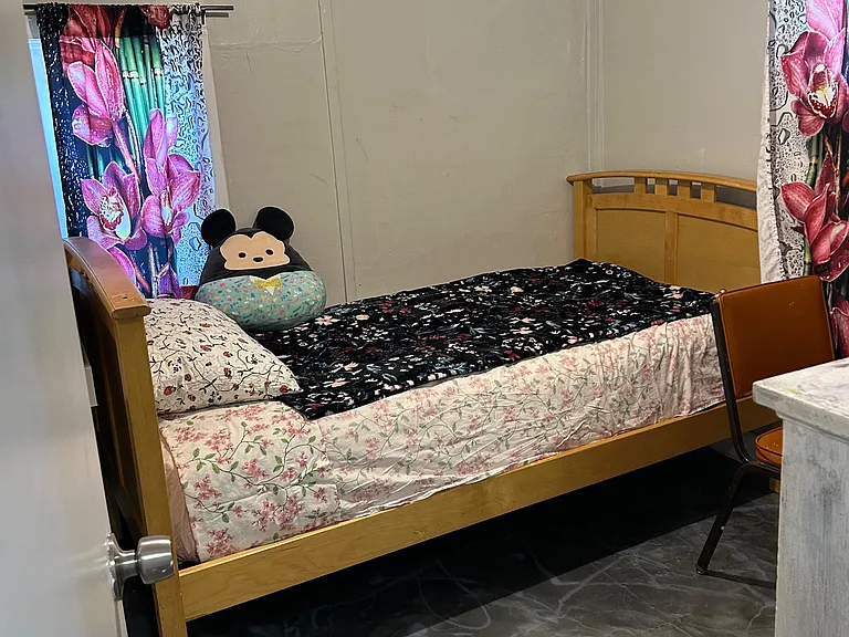 Furnished bedroom with a wood bed frame, patterned bedding, and two windows with curtains for natural light.