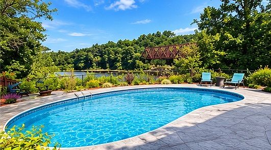 Resort-style outdoor living featuring an inground pool, expansive stamped concrete patio, and beautiful landscaping.