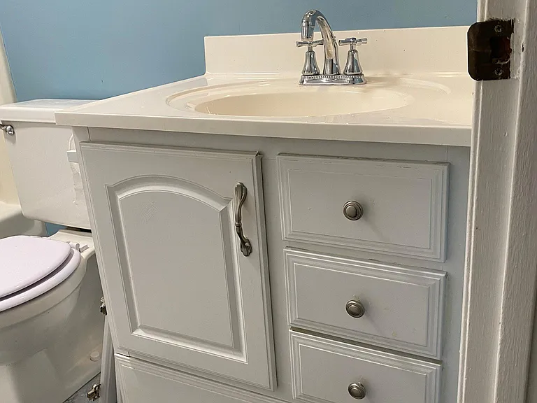 White composite top vanity with storage under sink and SURPRISE toe space drawer. 
Towel bar under the over toilet storage cabinet.