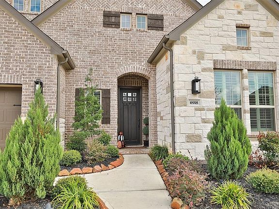 6918 Twilight Elm Trace offers a fantastic curb appeal with a beautiful brick and stone exterior, lush landscaping, ambient lighting, and a beautiful dark stained front door.