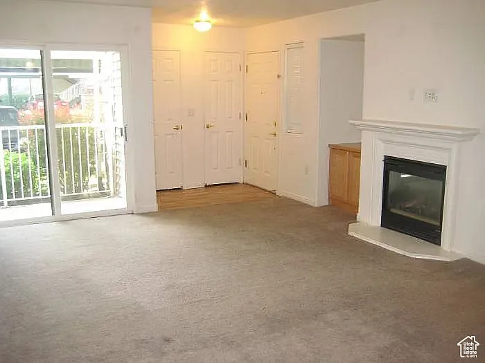 Unfurnished living room with a glass covered fireplace and light colored carpet