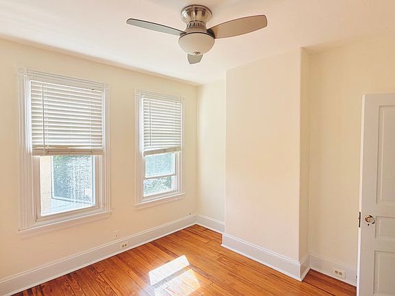 Cozy second bedroom with two windows, ceiling fan with light, hardwood floors, and a panel door with original hardware.