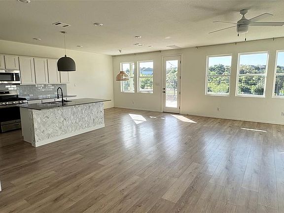 Kitchen featuring appliances with stainless steel finishes, white cabinets, open floor plan, backsplash, and a kitchen island with sink
