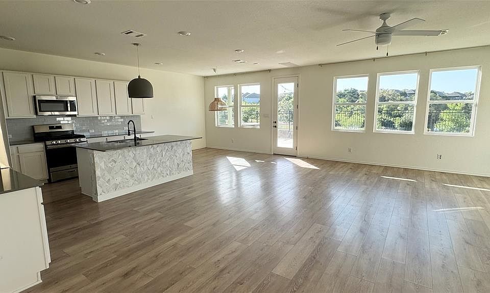 Kitchen featuring appliances with stainless steel finishes, white cabinets, open floor plan, backsplash, and a kitchen island with sink