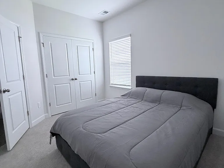 Private bedroom with a comfortable bed, window with blinds, and a double-door closet for storage.