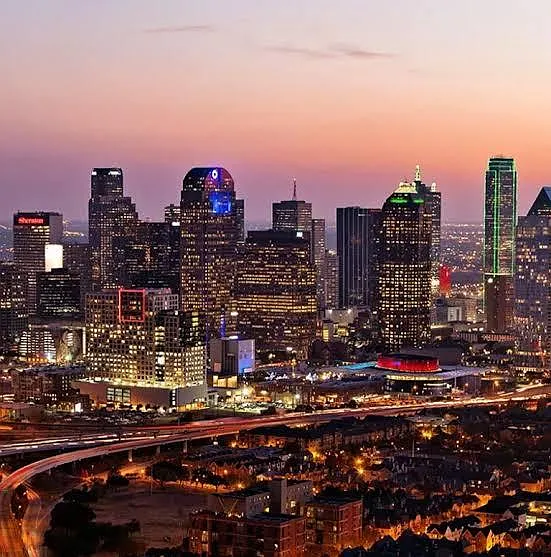 Panoramic downtown skyline view at dusk with illuminated high-rise buildings and highway in the foreground.