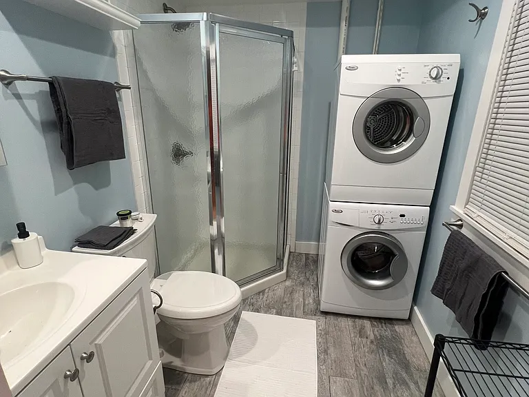 Full bathroom with glass-enclosed shower, full-size stacked washer and dryer, fresh towels and brand-new bath essentials.