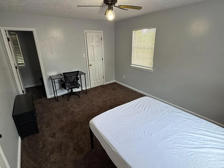 Private bedroom with a ceiling fan, carpeted flooring, and a window with blinds plus space for a desk or dresser.