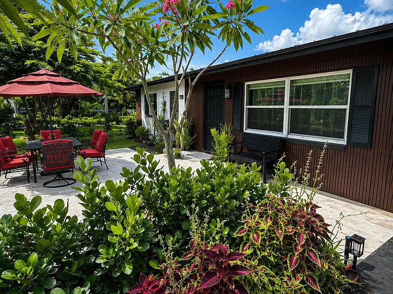 Tropical exterior view of this fully renovated Naples home featuring lush landscaping, flowering palms, a bright patio seating area, and convenient private parking for up to 6 cars_perfect for families, groups, and extended stays near Naples beaches.