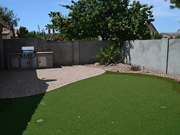back yard with grill island, synthetic grass, and pavers