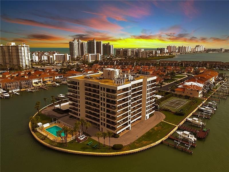 Looking West Northwest, onto the Sand Key Barrier Island, we have in the foreground the Harborage-1 property's 8-floors above ground building, its year round heated pool, yacht slips/docks & tennis courts, with the Intracoastal Waterways, Barrier Island a