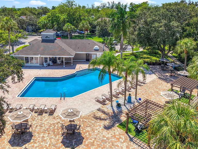 This vibrant bird's-eye view shows off the beautifully maintained pool deck, shaded seating areas, and lush greenery that define River Reach's outdoor oasis.
