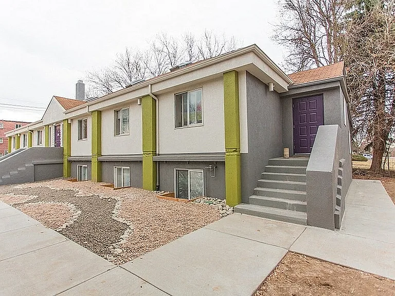 Charming modern apartment building with vibrant accents and inviting entrance, surrounded by a tidy xeriscape garden.