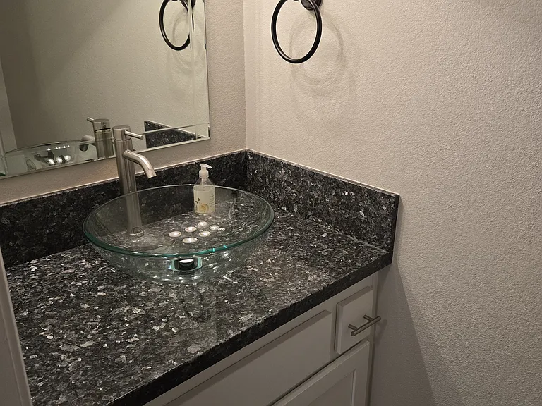 Beautifully remodeled powder room featuring granite countertops, a designer glass vessel sink, and contemporary fixtures.