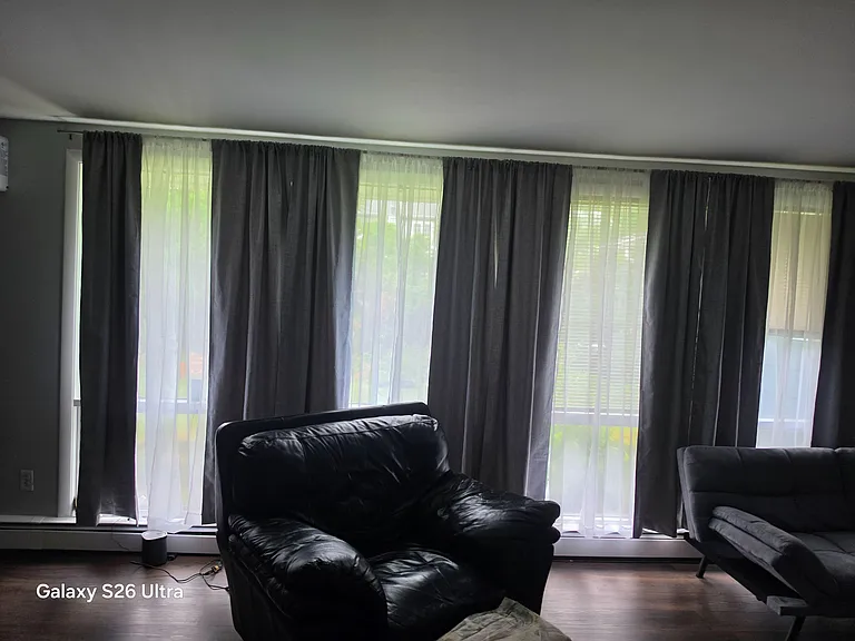 Living room with multiple large windows, layered curtains, and seating space for lounging or entertaining.