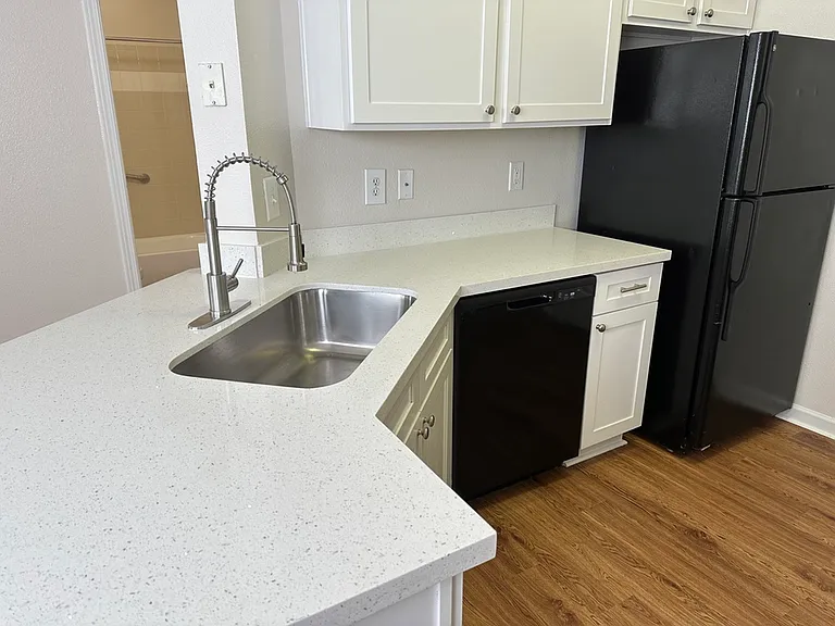 Modern kitchen with sleek quartz countertops, stainless steel sink, and elegant cabinetry, featuring a black refrigerator and dishwasher, set against chic wood-style flooring. Modern kitchen with sleek quartz countertops, stainless steel sink, and elegant