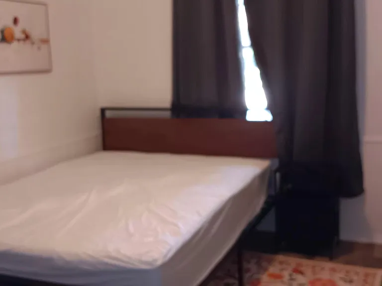 Private furnished bedroom with a queen-size bed, window with blackout curtains, wardrobe, dresser for storage & a work area.