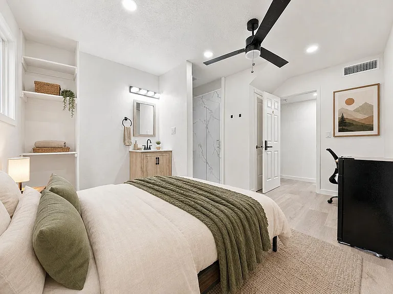 Spacious bedroom with ceiling fan, built-in shelving, a desk nook, and an en-suite bath with walk-in shower.