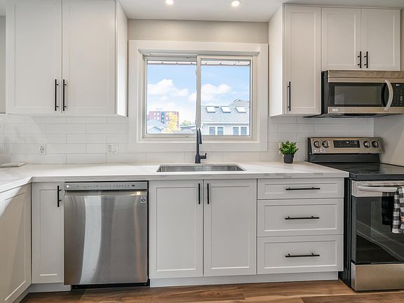 Note stainless steel dishwasher, oven/stove, microwave. Fridge is behind you. Beautiful, clean, flawless white tile backsplash. Large corner cabinet to left of dishwasher. Window looks to backyard