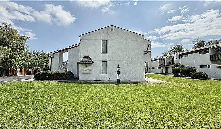 Charming apartment complex with fresh white facade, nestled in a lush green landscape under a bright blue sky.