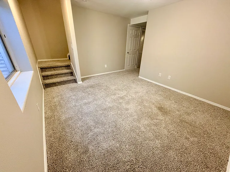 Spacious lower-level family room offering a flexible second living area with natural light and convenient access to the third bedroom, full bathroom, laundry room, and under-stair storage.