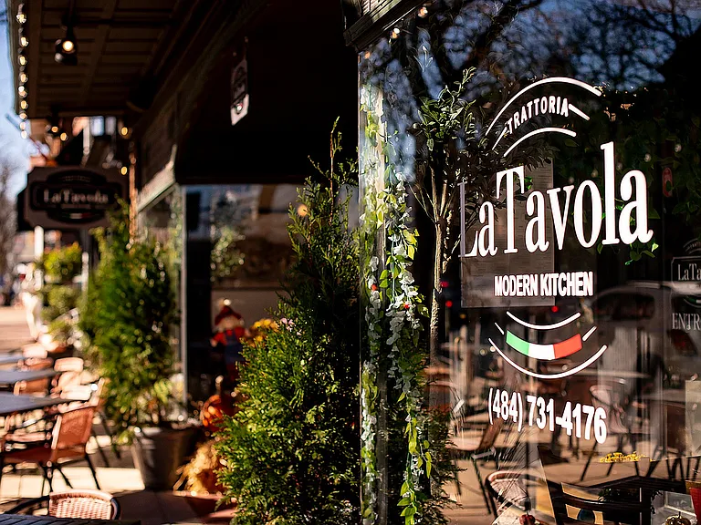 Experience the inviting atmosphere of La Tavola, featuring cozy outdoor seating surrounded by vibrant greenery.