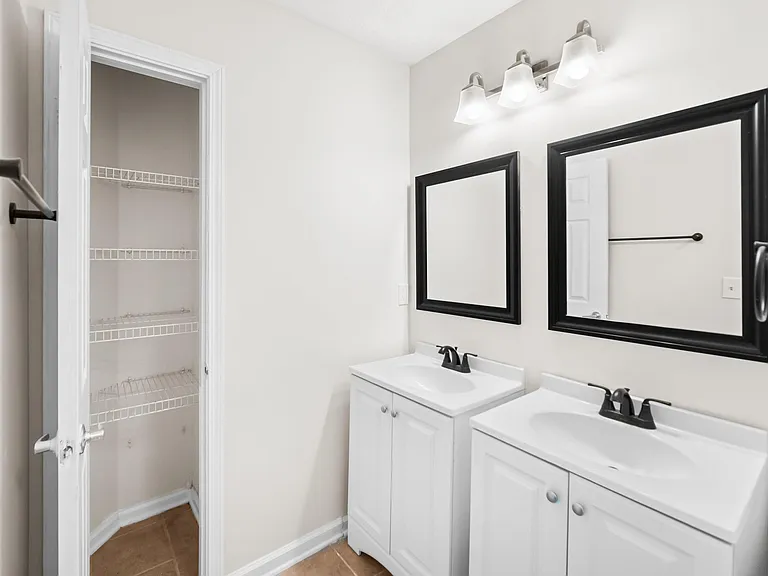 Bathroom with a dual-sink vanity, framed mirrors, and ample storage including a large linen closet.