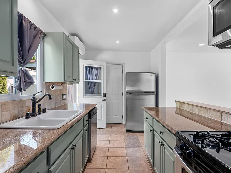 Kitchen with air conditioning unit, stainless steel refrigerator, and pull down ironing board.