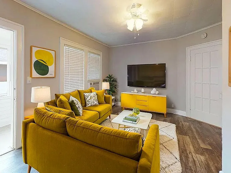 Charming living room with vibrant yellow sofas, modern decor, and a sleek TV setup creating a cozy, stylish ambiance.