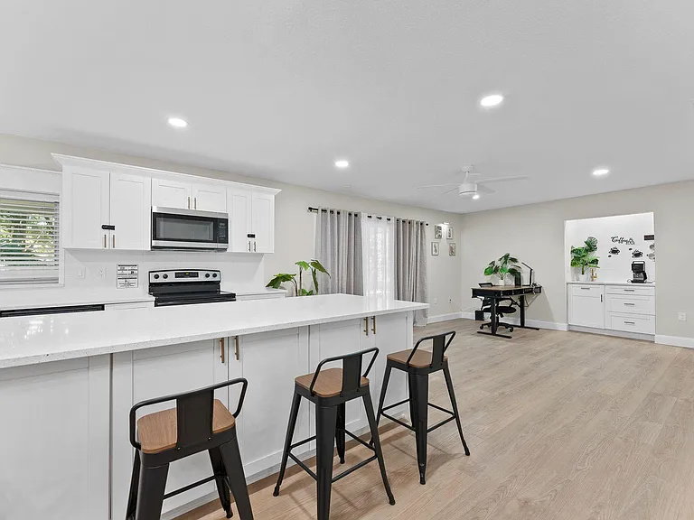 Open kitchen with oversized island seating, ample white cabinetry, and nearby flexible space for dining or a home office.