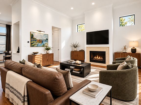 Elegant, light-filled living room featuring soaring ceilings, a cozy gas fireplace, a large wall-mounted TV, and thoughtfully curated furnishings. Designed for comfortable, upscale living.