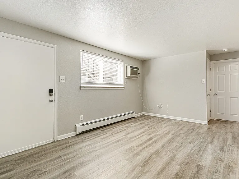 Bright and airy room with stylish laminate flooring, featuring a large window and modern air conditioning unit.