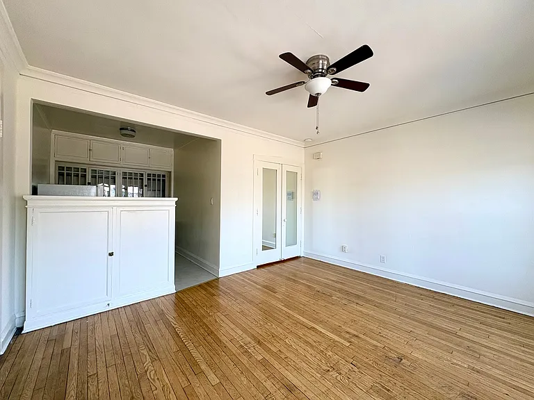 Bright and spacious living room with elegant hardwood floors, a classic ceiling fan, and built-in cabinets in an inviting open layout. Bright and spacious living room with elegant hardwood floors, a classic ceiling fan, and built-in cabinets in an invitin