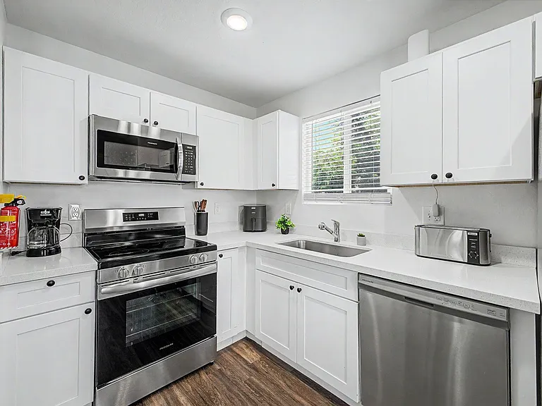 U-shaped kitchen with ample cabinet storage, quartz-look counters, and stainless appliances plus a window over the sink.