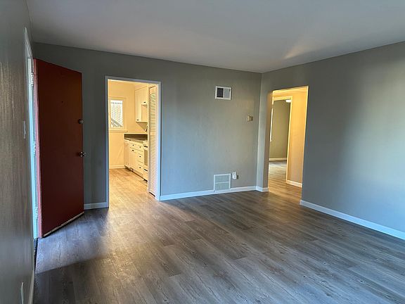 Living room with view of open front door, kitchen entry and hallway to bedrooms / bath