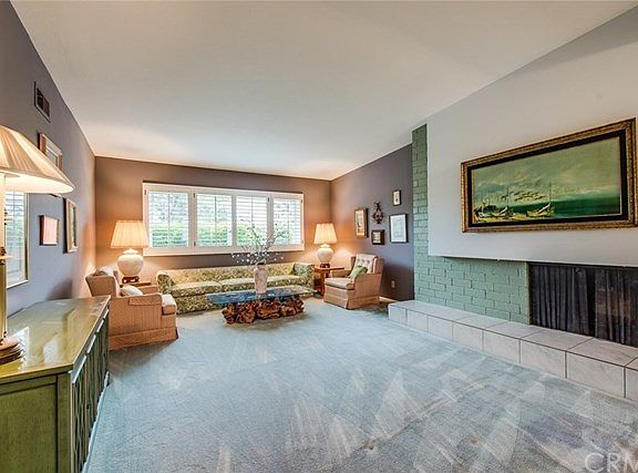 The living room features plantation shutters & a fireplace with raised tile and brick hearth.