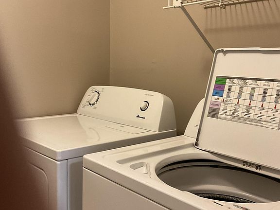 Laundry room with washer and dryer. Shelving on opposite wall.