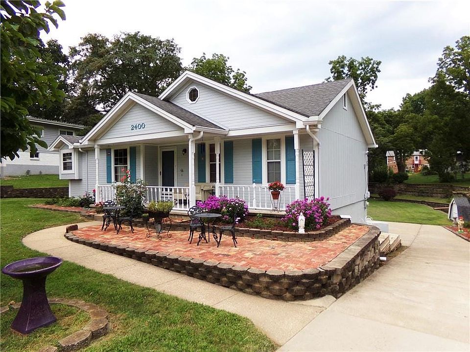 Light blue siding exterior with a covered front porch, a bay window, and a brick paver patio with a raised garden bed