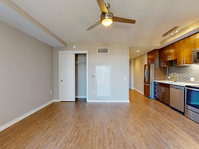 Apartment kitchen with stainless steel appliances, dining and living room with wood-style flooring.