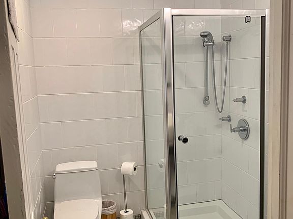 Renovated Master Bathroom with overhead rain shower, modern basin sink, new commode, floor to ceiling wall tile, heated tile floors, and window allowing natural light.