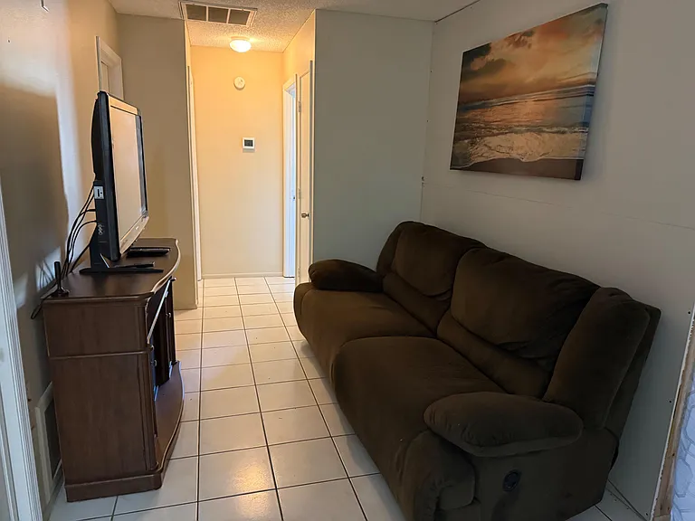 Compact common lounge with tiled floors, a comfortable sofa, and a TV setupideal for relaxing between errands.