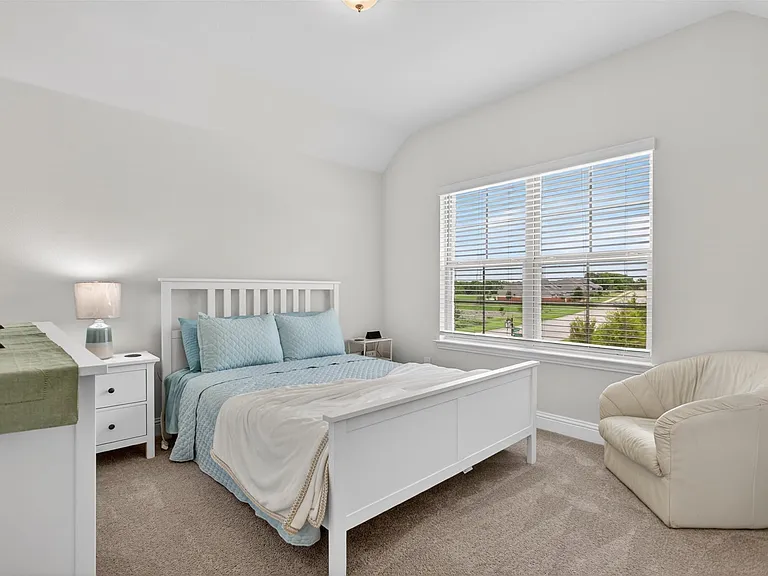 Carpeted bedroom featuring a large window with horizontal blinds, white painted walls, and a built-in ceiling light fixture